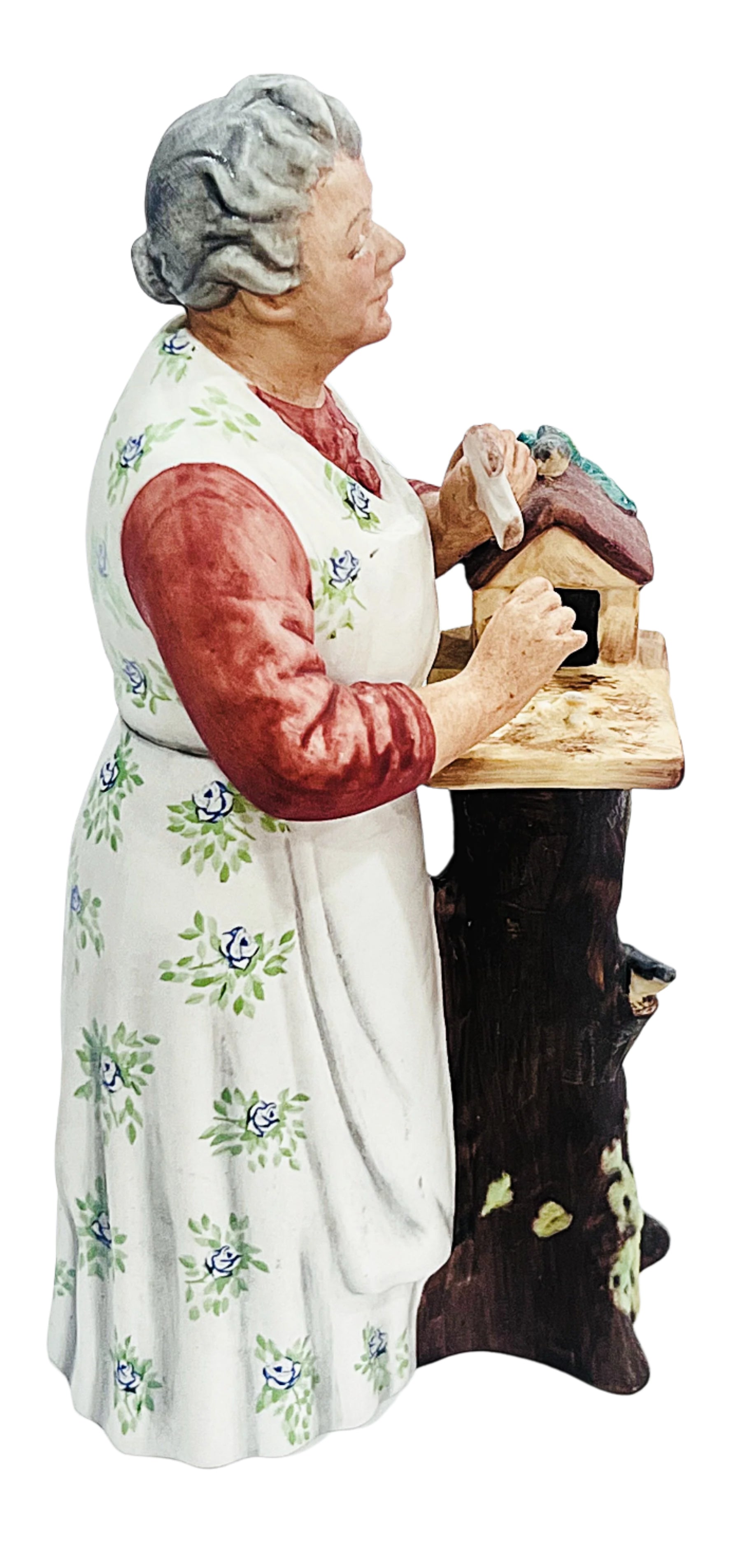 Statue of an elderly woman with a floral apron holding a wooden block feeding a bird.