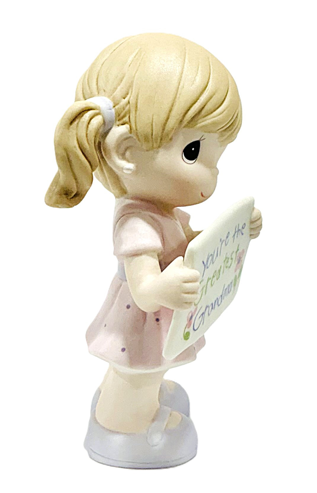 A Precious Moments figurine of a young blonde girl with a ponytail, wearing a light pink dress, holding a sign that reads 'You're the greatest Grandma!'.