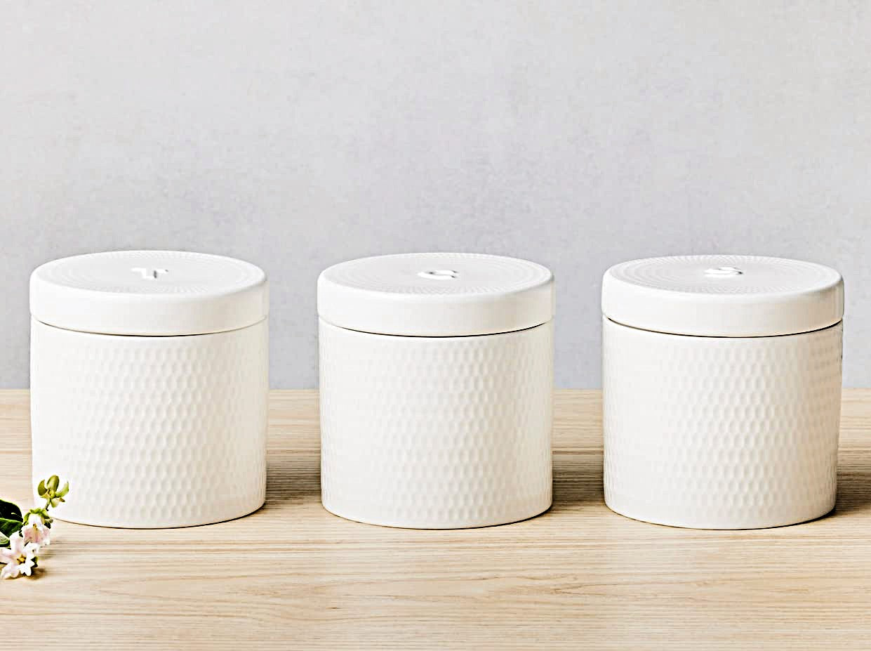 Three white textured ceramic jars on a wooden surface with a light gray background
