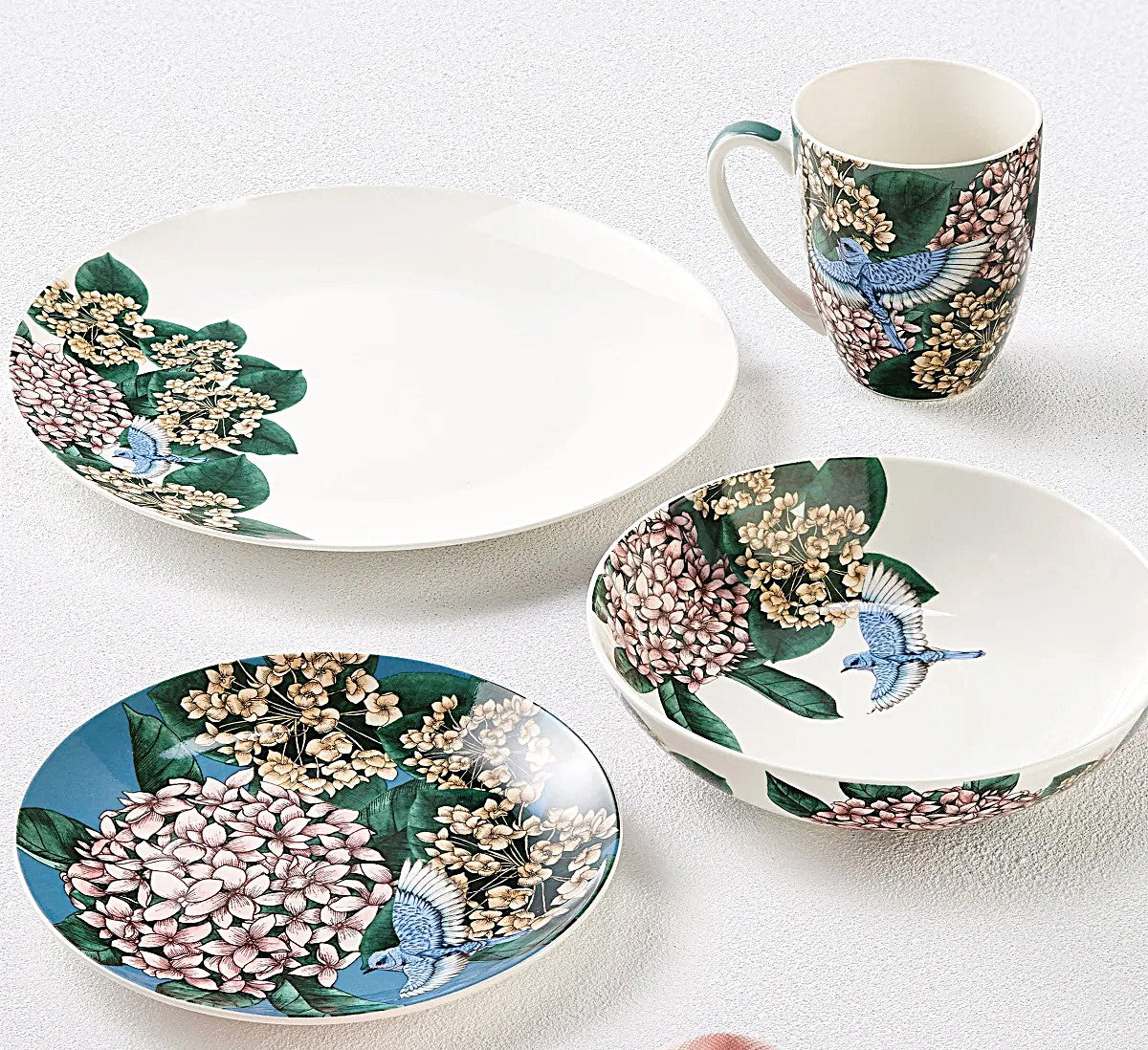 Set of ceramic plates and a mug with floral and bird design on a white background
