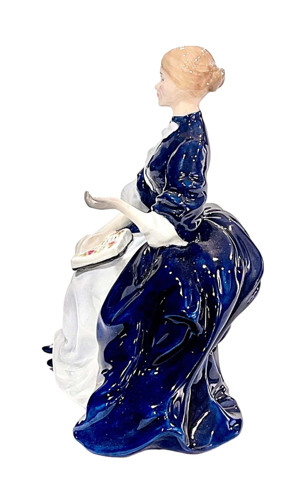 Bone china figurine of a woman in a blue dress sitting on a white chair with a white cushion.